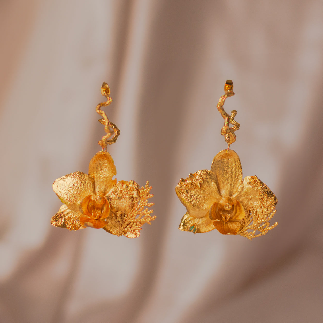 Aretes Candonga Orquidea Phalaenopsis Pino Esmeralda en bronce bañado en oro de 24k, destacando la belleza única de las flores y hojas inmortalizadas con detalles de esmeralda.