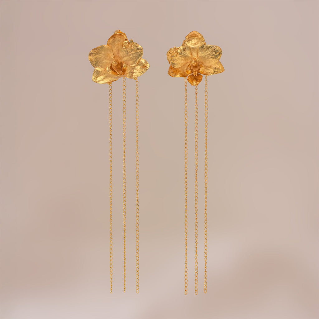 Aretes dorados compuestos por una orquídea Phalaenopsis en el lóbulo y una fina cadena colgante que aporta movimiento.