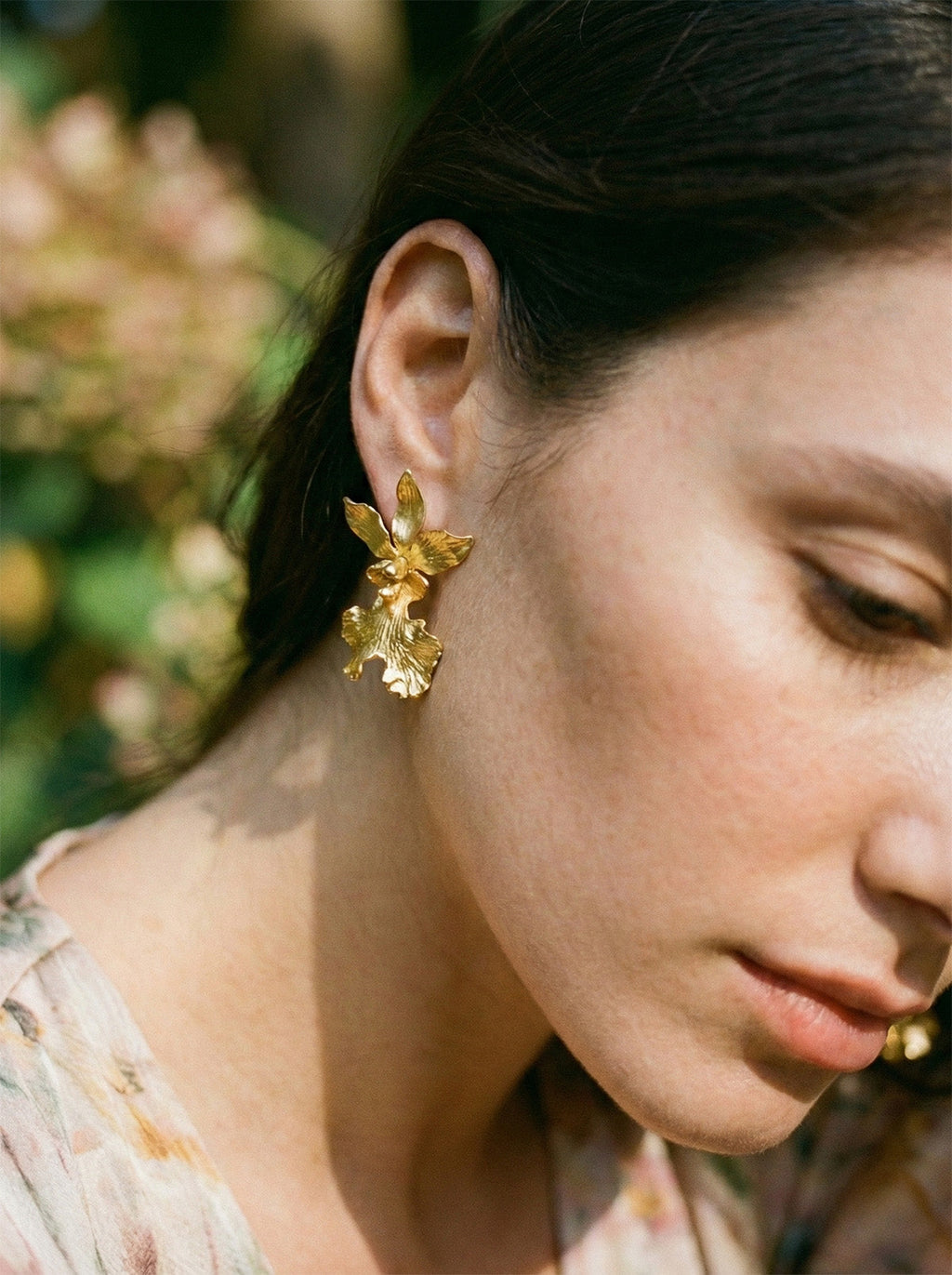Detalle de aretes florales elegantes, orquídea andina preservada en oro con diseño de movimiento natural.