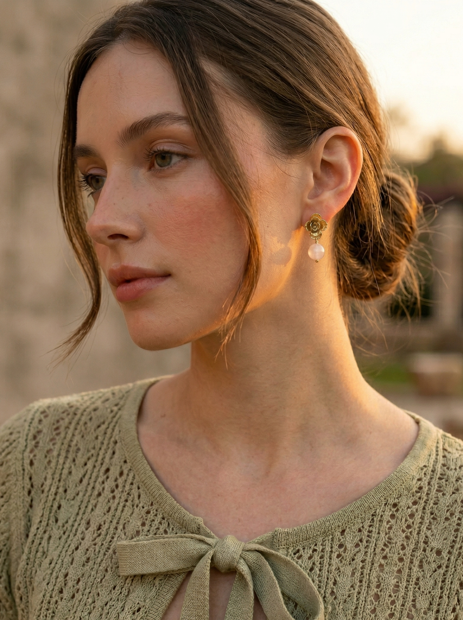 Pendientes de suculenta natural bañada en oro 24k con cuarzo, sostenidos en la mano frente a ventana en Madrid, joyería botánica colombiana Liz de la Cruz