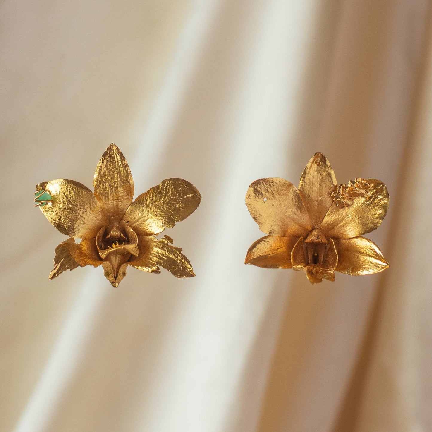 Close-up of Dendrobium Orchid Emerald Elderberry Earrings with bronze orchid petals, 24k gold plating, and emerald accents