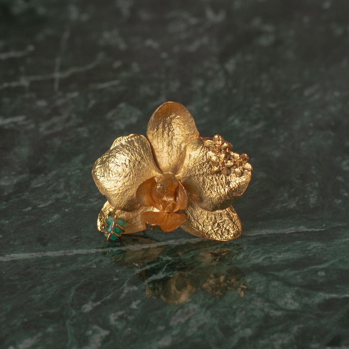 Close-up of Phalaenopsis Orchid Elderflower Emerald Ring, showcasing the intricate details of the orchid preserved in bronze and enhanced with 24k gold plating and a Colombian emerald